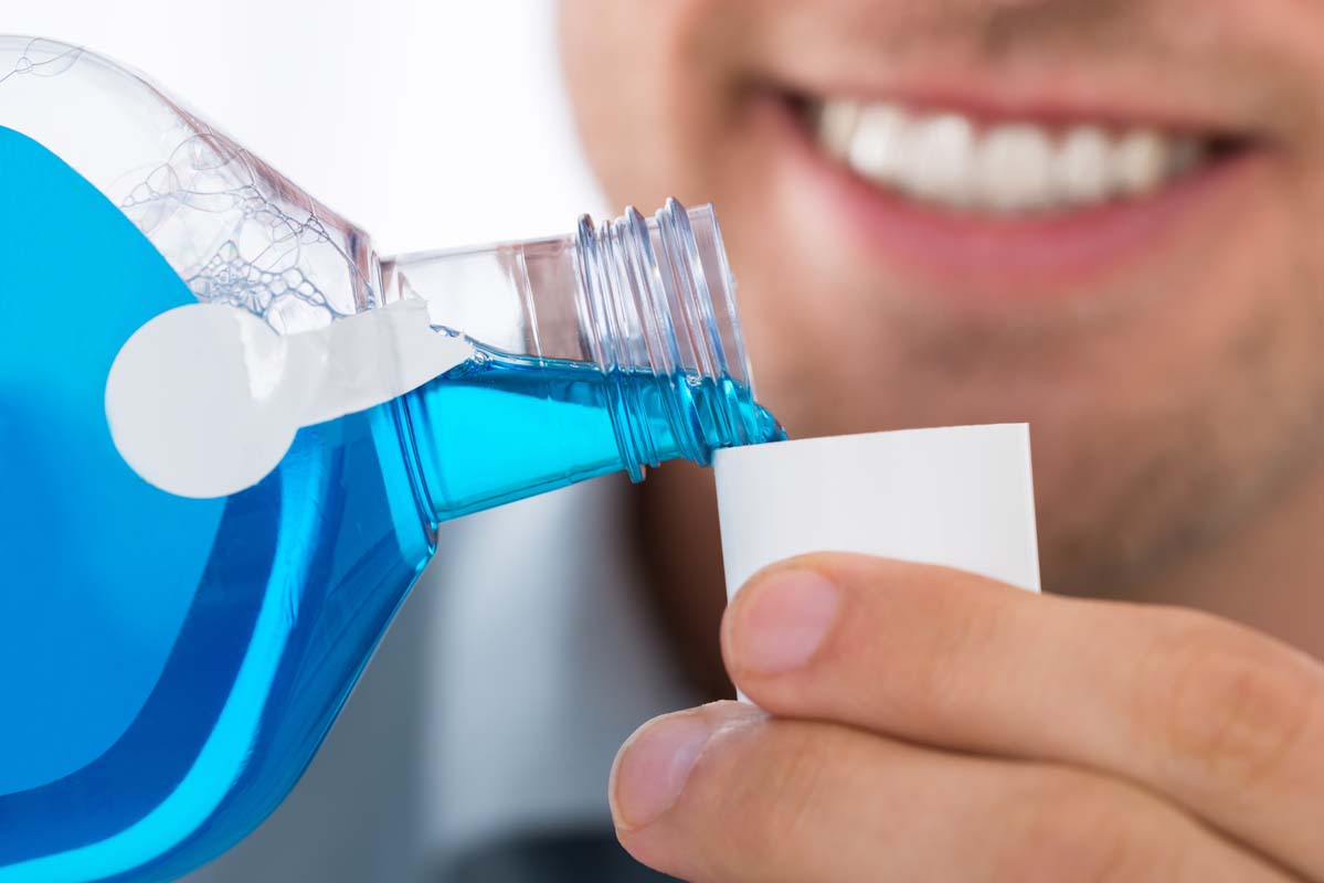 smiling man pouring mouthwash into a small cup
