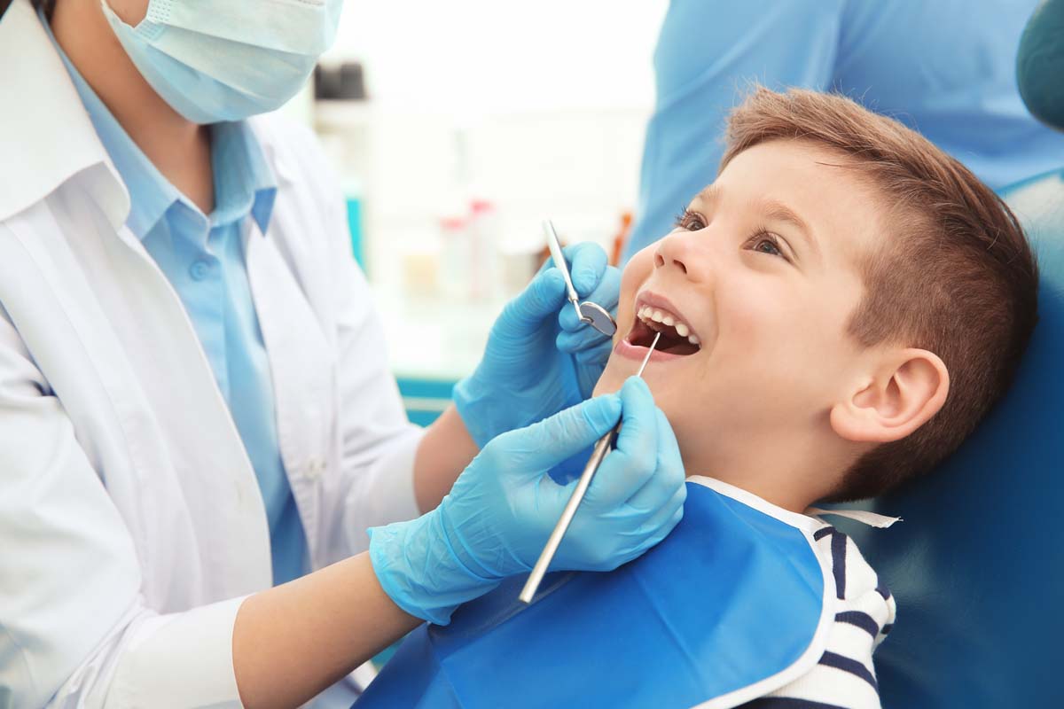 small child in dentist chair smiling while dentist performs exam