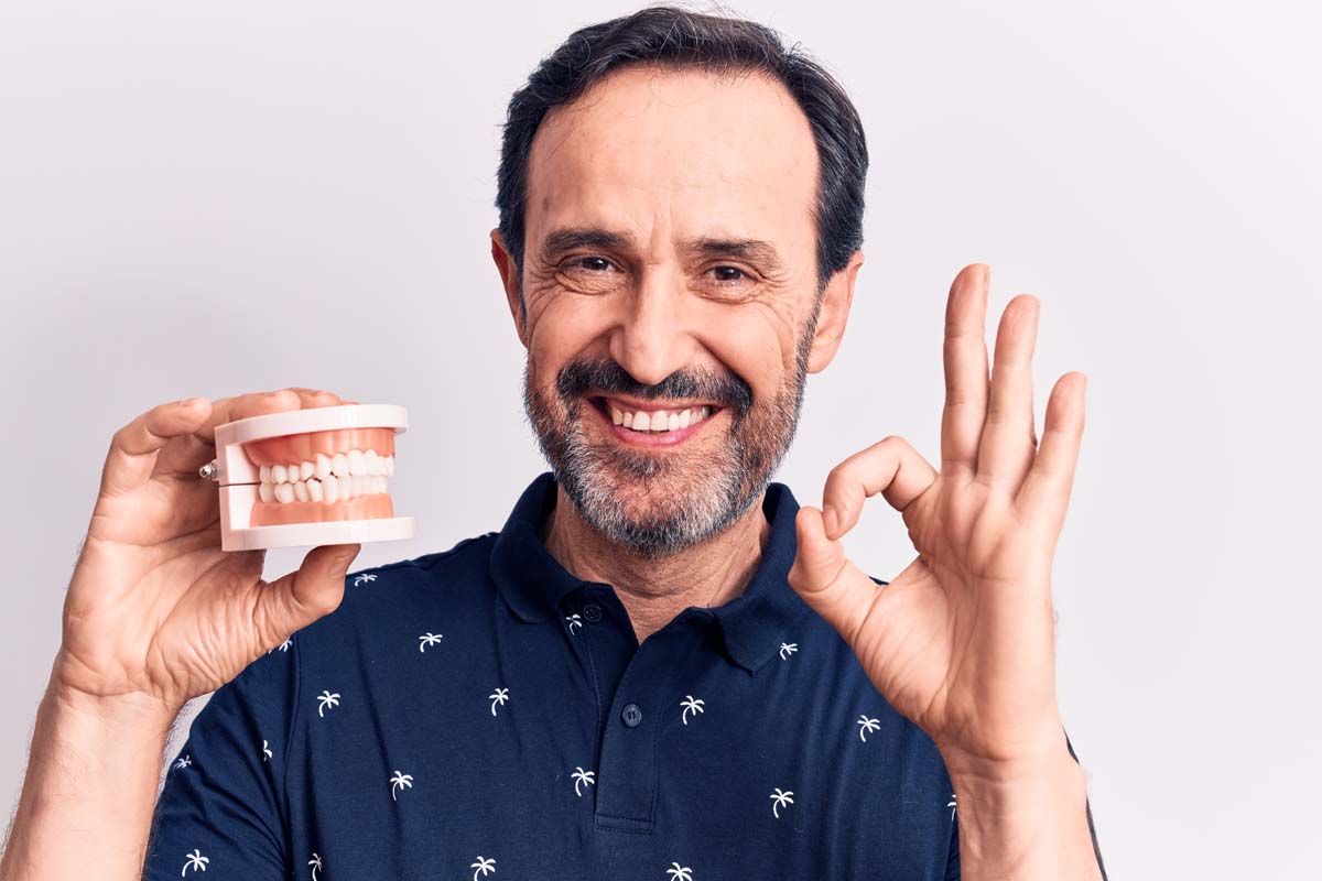 smiling man holding dentures and giving ok sign