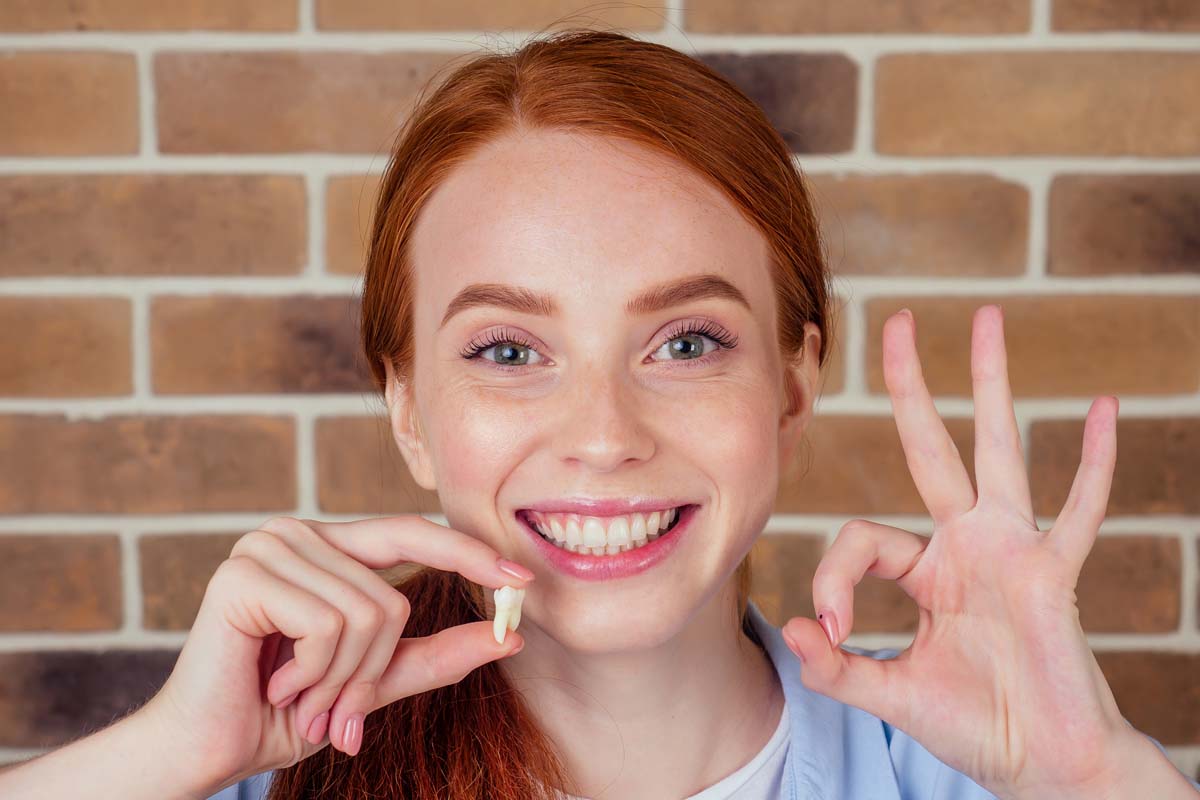 woman holding tooth ok sign smiling after tooth extraction