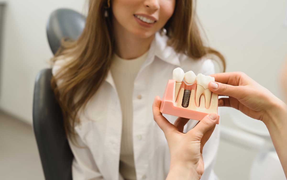 First person shot female doctor talking to a young woman patient. Discussion of the treatment plan. The dentist shows a model of a dental implant
